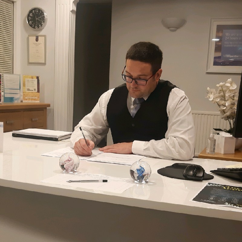 Kevin at a desk, in undertakers uniform.